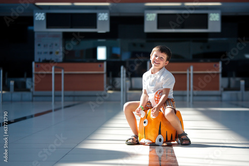 Cute little boy with orange suitcase at airport