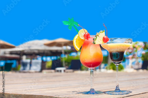 two glasses of bright cocktails near pool on clear blue sky