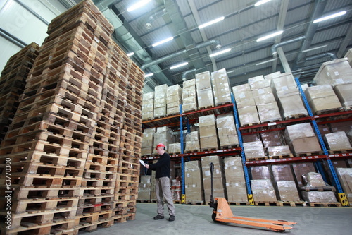 worker with order at stack of wooden pallets in storehouse photo