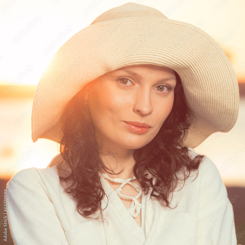 Woman wearing straw hat smiling and having fun against sunset an