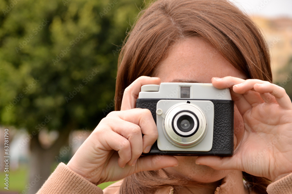 Young woman taking pictures with an old camera in the park Young woman taking pictures with an old camera in the park