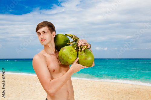 Happy handsome young male beach holding coconuts under the sun o