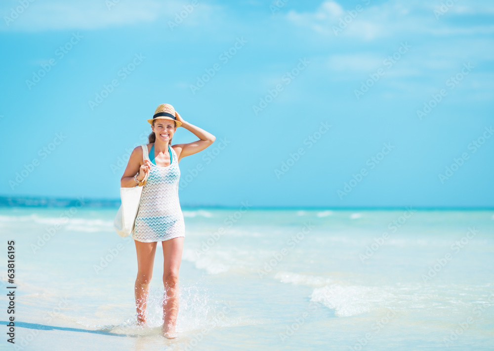 Happy young woman in hat with bag walking at seaside