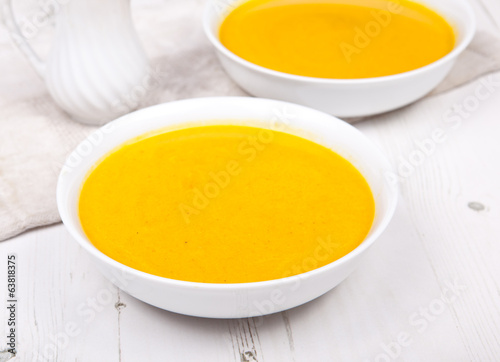 Carrot soup in two bowls, on the white table