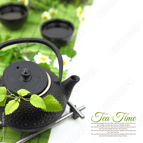 Teapot with fresh green herbs, flowers, cups and copy-space