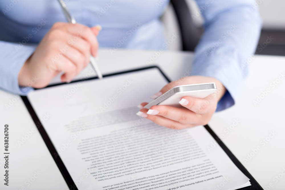 Young woman working with a mobile phone and holding a pen