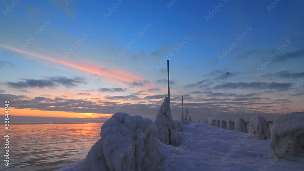 Frozen pier and ocean at sunrise light with flying seagulls Frozen pier and ocean at sunrise light with flying seagulls