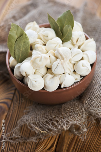 Glass bowl with raw pelmeni and dry bay leaves  vertical shot