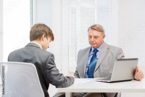 older man and young man signing papers in office