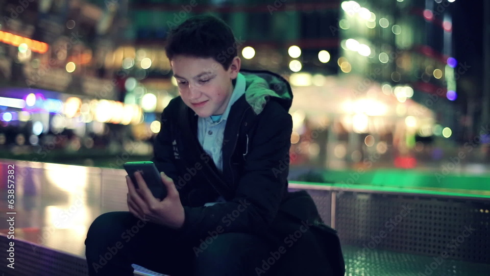 Young teenager texting on smartphone in the city at night