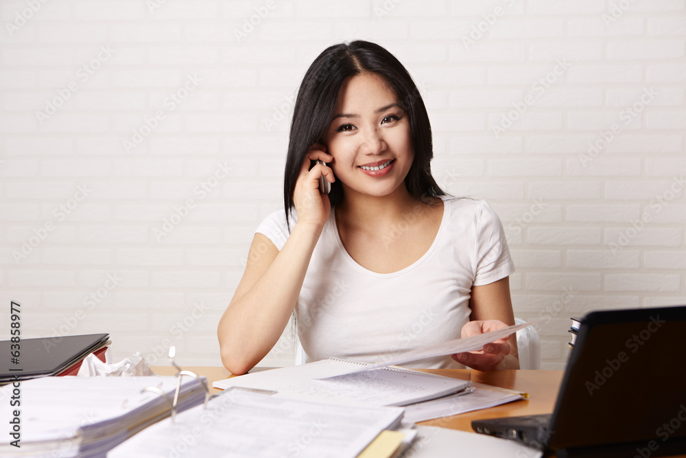 Studentin sitzt am Schreibtisch und telefoniert Studentin sitzt am Schreibtisch und telefoniert