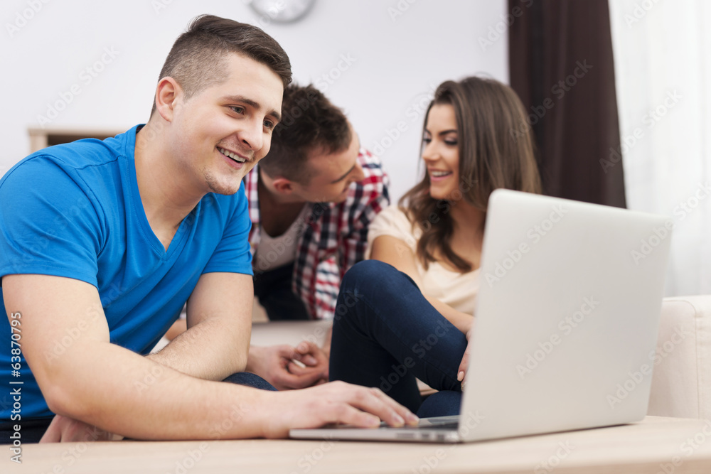 Smiling man using laptop with friends at home Smiling man using laptop with friends at home