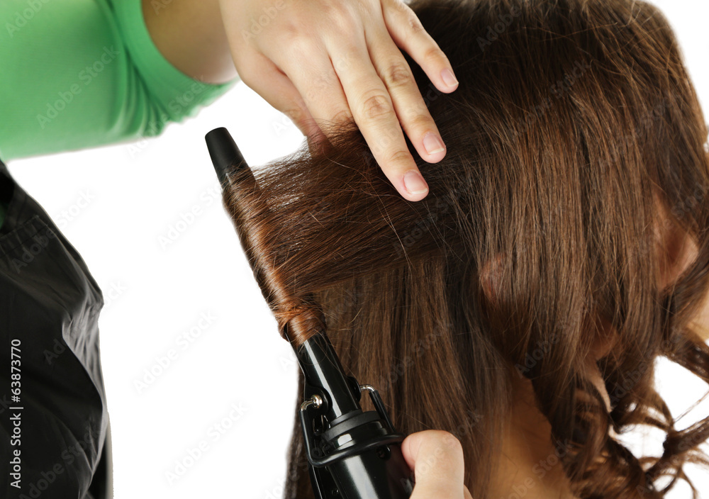 Naklejka premium Stylist using curling iron for hair curls, close-up, isolated