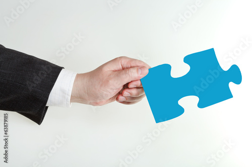 male hand holding blue puzzle piece on grey background