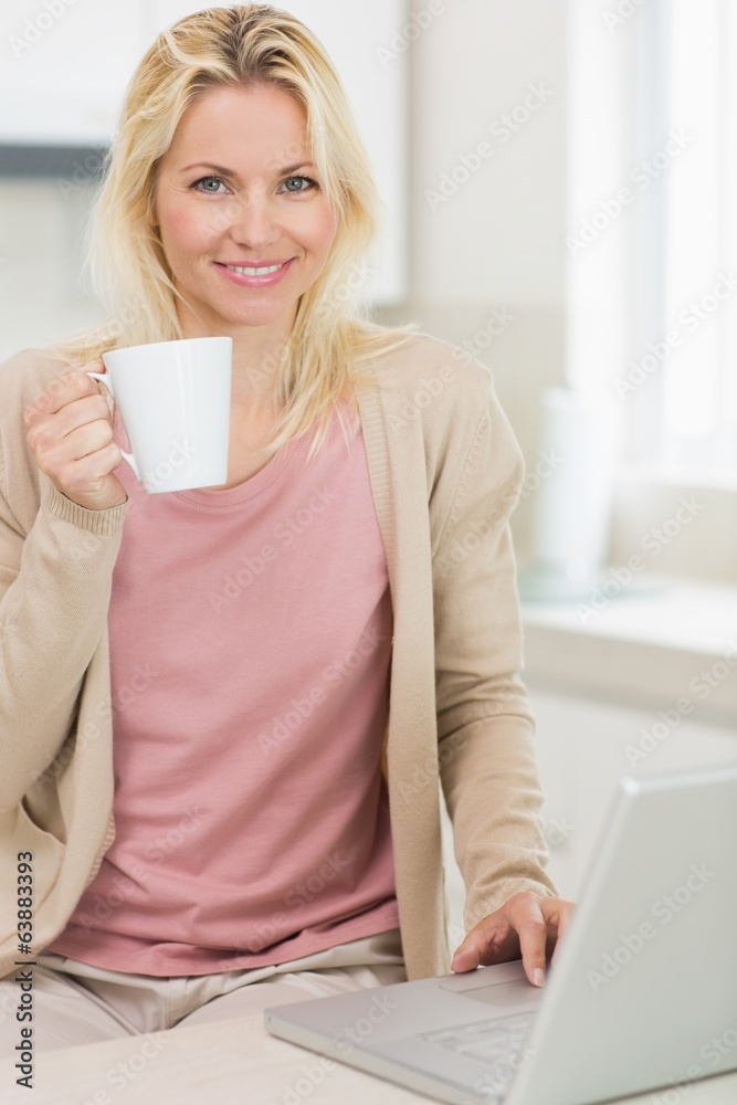 Beautiful woman with coffee cup using laptop in the kitchen Beautiful woman with coffee cup using laptop in the kitchen