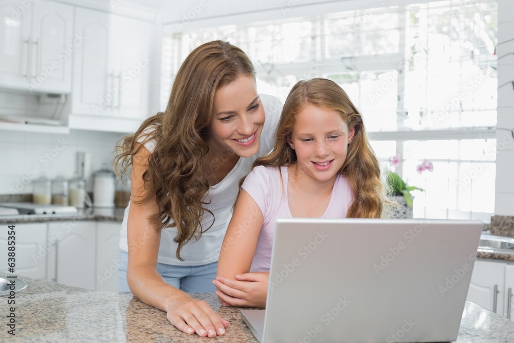 Happy mother and daughter using laptop in kitchen Happy mother and daughter using laptop in kitchen
