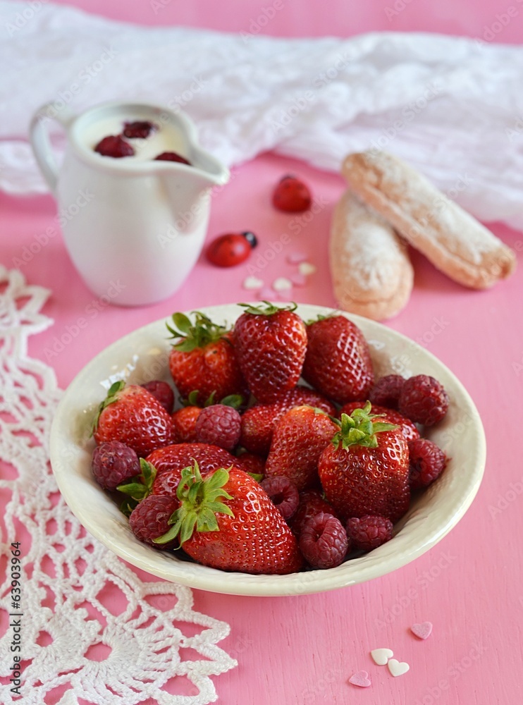 Strawberries and raspberries in a plate on pink background