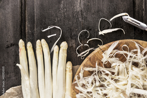 Shelled white asparagus with peelings on dark wooden table
