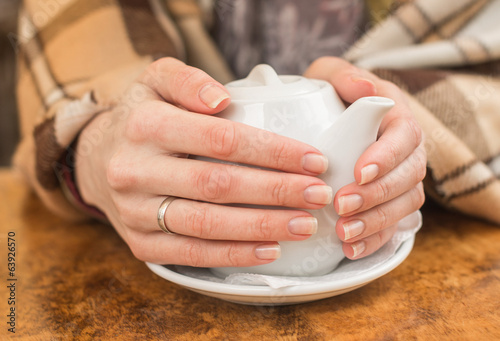 Woman wrapped in plaid warming hands with a teapot