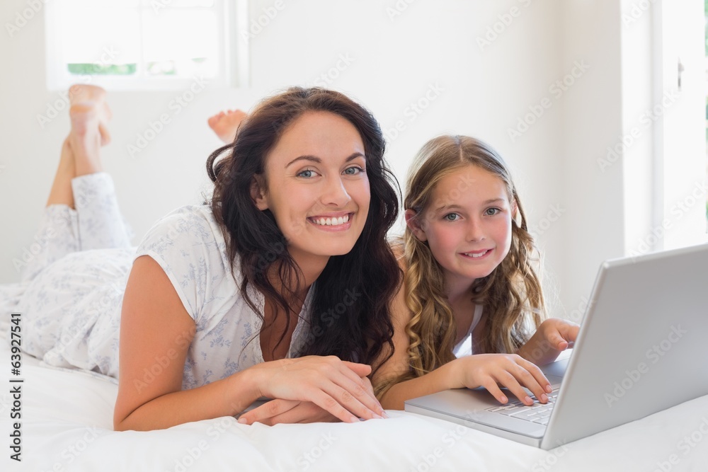 Mother and daughter with laptop lying in bed