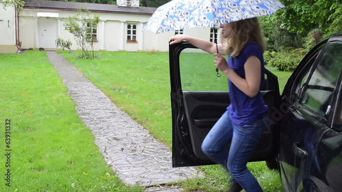 Girl with umbrella get out from car and walk cobble path in rain