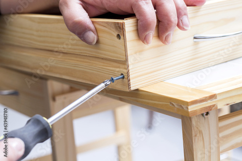 A carpenter builds a small white table with a screwdriver photo