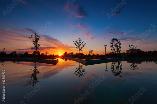 Reflection of sunrise, silhoutte of trees and wheel over a lake