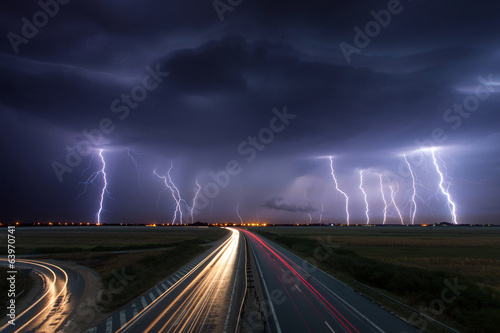 Thunderstorm and lightnings in night over a highway with car lig
