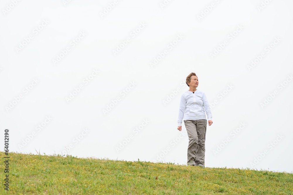 白い空をバックに芝生の上でストレッチ運動をする高齢の日本人女性