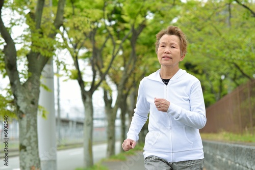 新緑の木々が植えてある歩道を健康のためにジョギングしている高齢のアジア人女性