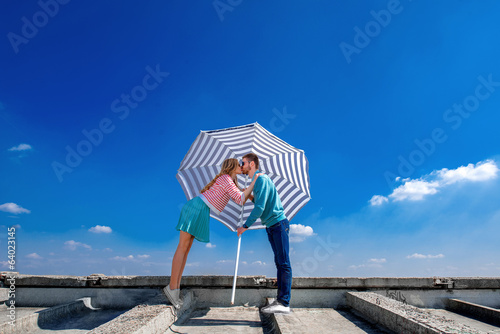 Young and pretty couple kissing on the roof under the umbrella o