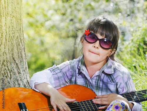 Happy little girl with glasses playing guitar outdoor