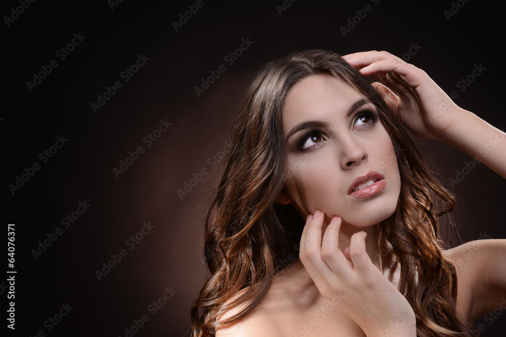 Fototapeta premium Beautiful young woman with long hair on dark brown background