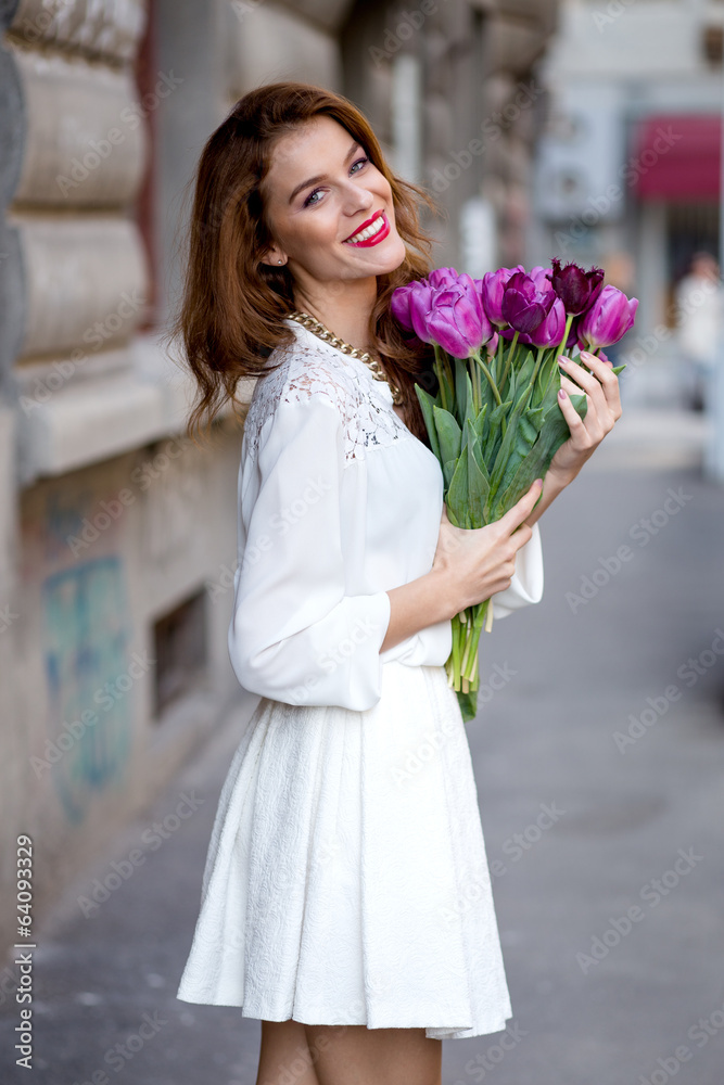Fototapeta premium Cute girl in white dress and a beautiful bouquet of tulips.