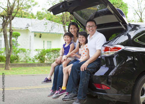 happy family sitting in the car and their house behind