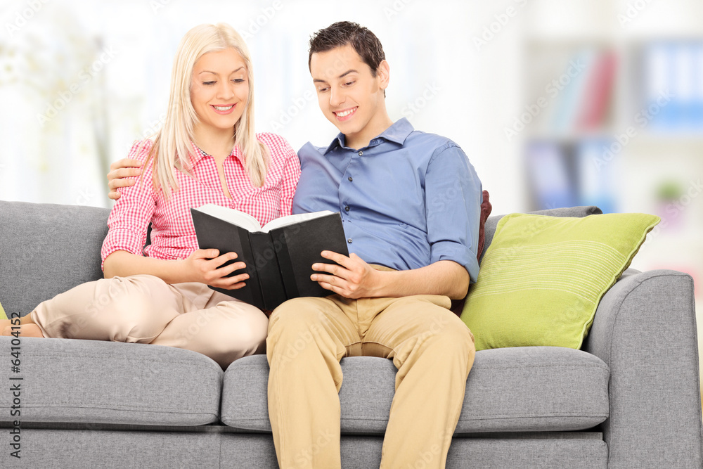 Man and woman reading a book seated on sofa