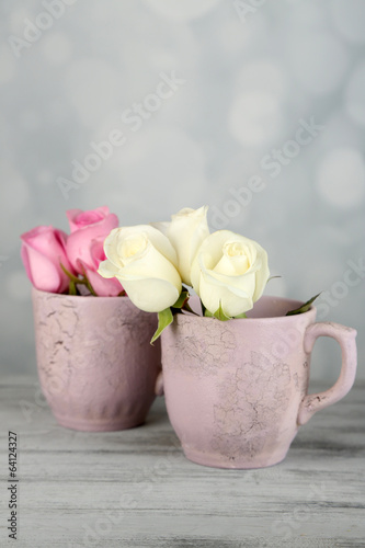 Beautiful roses in cups on light background