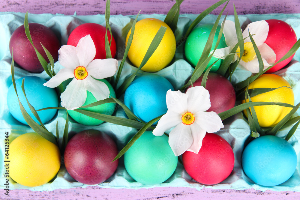 Colorful Easter eggs with grass and flowers in tray Colorful Easter eggs with grass and flowers in tray