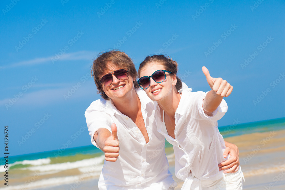 happy young couple on beach smiling and hugging. Thumbs up happy young couple on beach smiling and hugging. Thumbs up