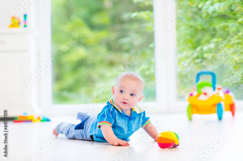 Cute baby boy with colorful ball and toy car next big window