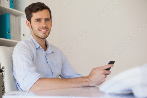 Casual happy businessman sending a text at his desk