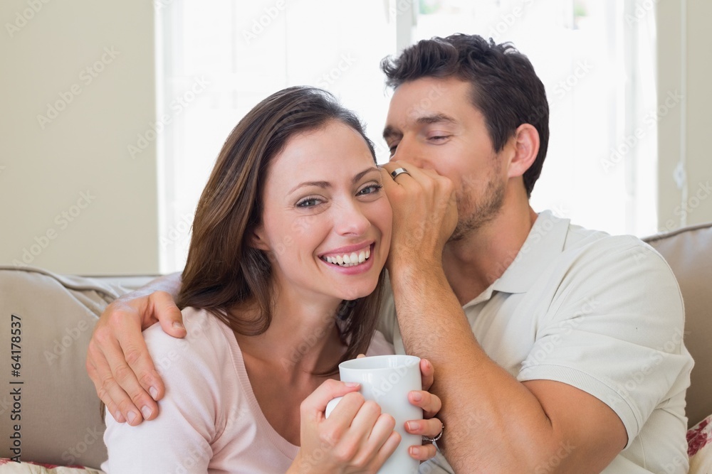 Man whispering secret into a womans ear in living room Man whispering secret into a womans ear in living room