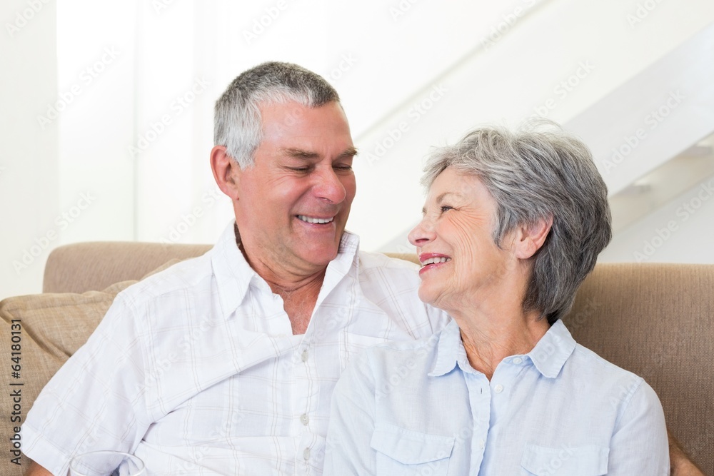 Senior couple sitting on sofa smiling at each other Senior couple sitting on sofa smiling at each other