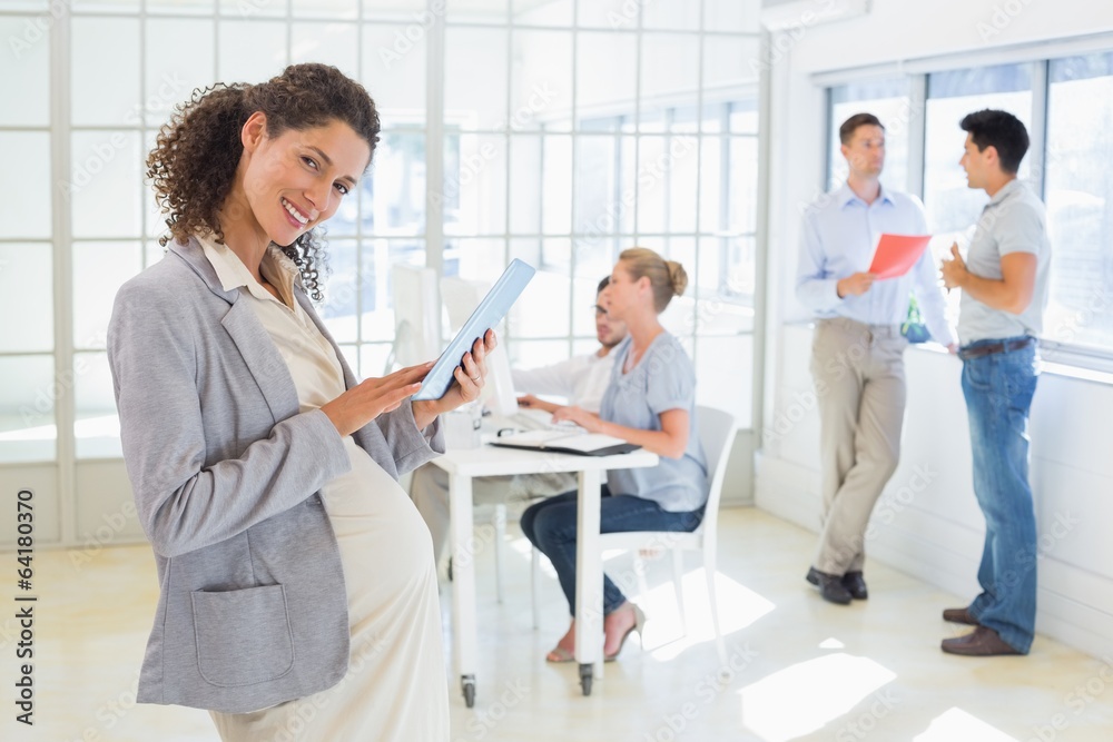Pregnant businesswoman using tablet with team behind her Pregnant businesswoman using tablet with team behind her