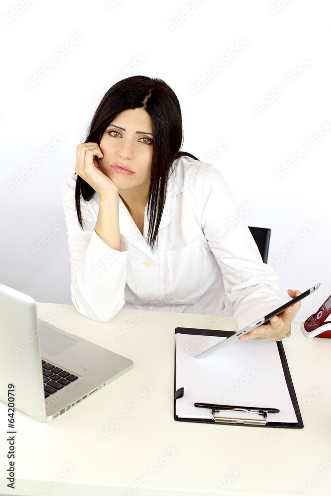Unhappy bored female doctor at work on desk with technology Unhappy bored female doctor at work on desk with technology