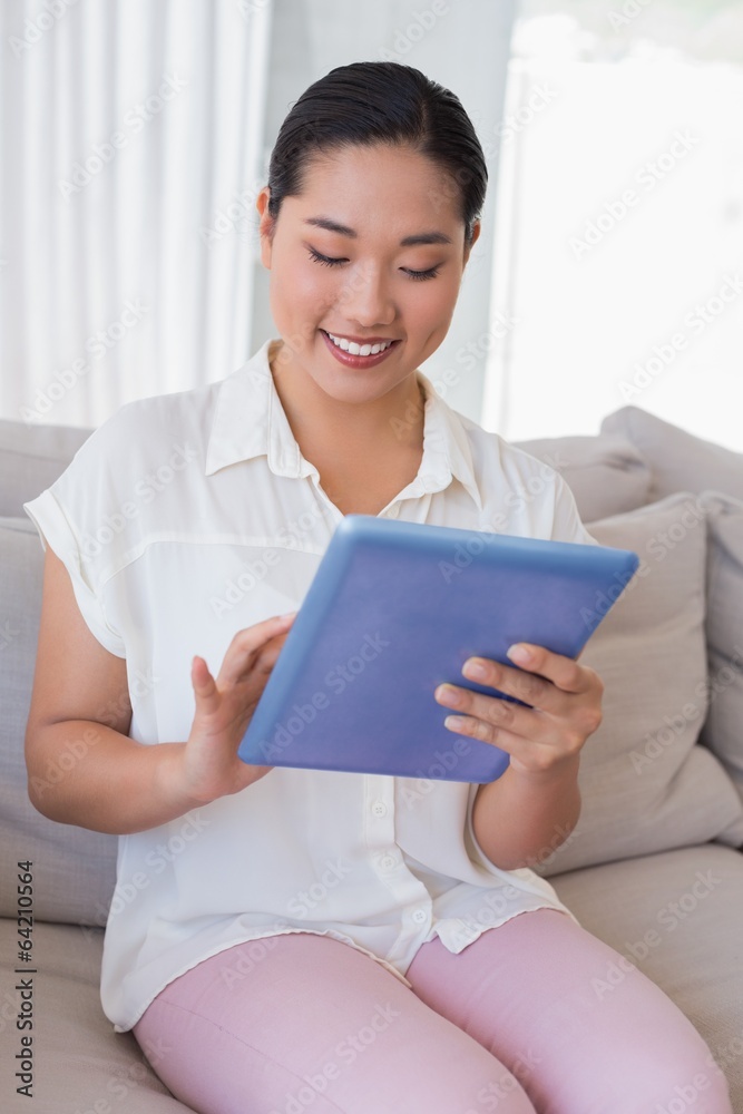 Smiling woman sitting on couch using tablet pc Smiling woman sitting on couch using tablet pc