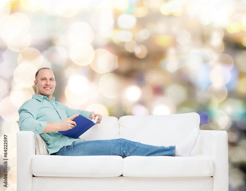 Obraz premium smiling man lying on sofa with book