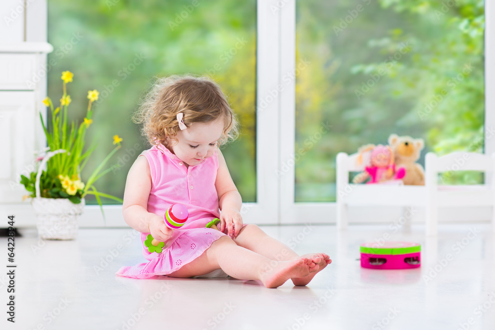 Funny curly toddler girl playing tambourine in sunny white room Funny curly toddler girl playing tambourine in sunny white room