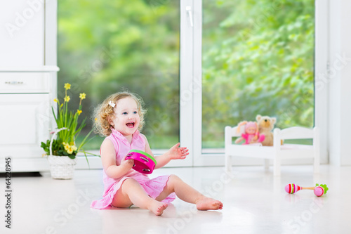 Little toddler girl playing tambourine in white nursery