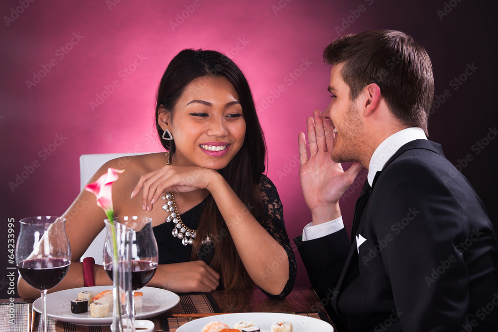 Man Whispering In Woman's Ear At Restaurant Man Whispering In Woman's Ear At Restaurant